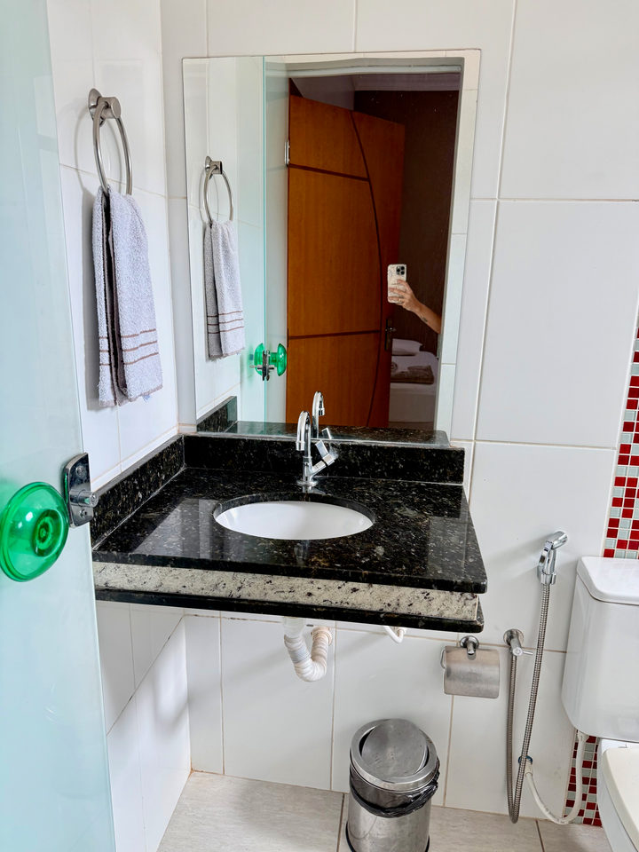 Banheiro com bancada de granito, cuba branca e espelho
