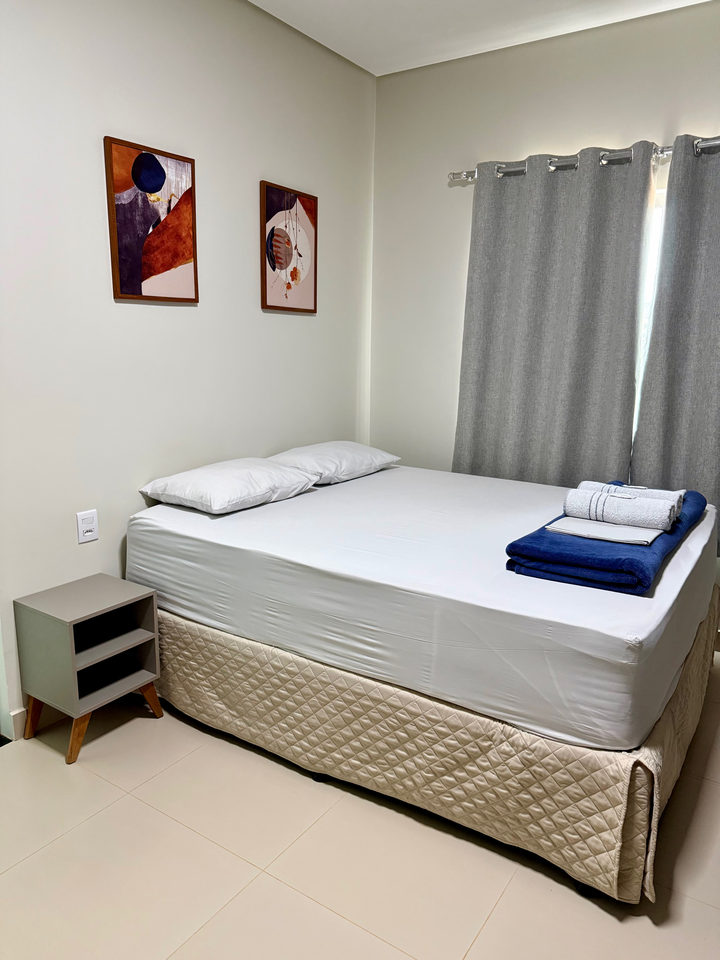 Cama queen com dois quadros, criado-mudo e toalhas azuis