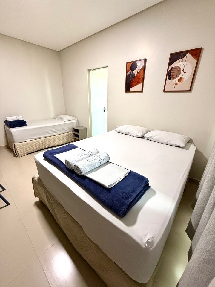Cama queen com enxoval azul e cama de solteiro, com quadros na parede