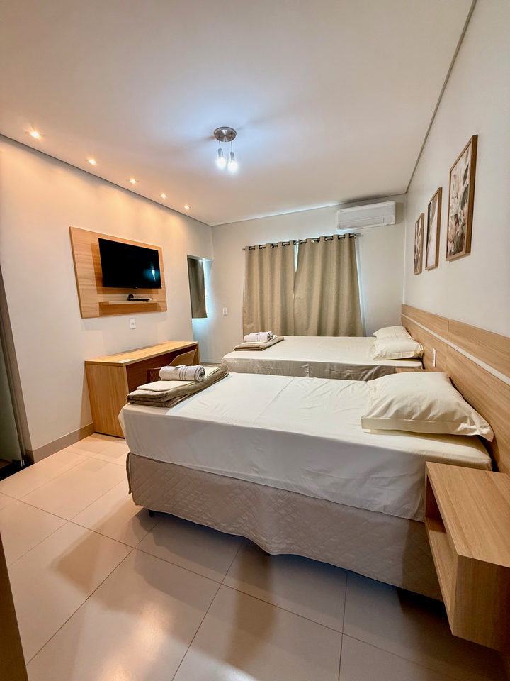 Apartamento com televisão no painel, cama queen e cama de solteiro