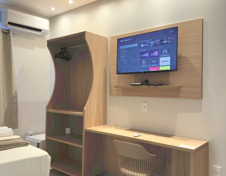 Painel de madeira com televisão, guarda-roupa aberto e escrivaninha
